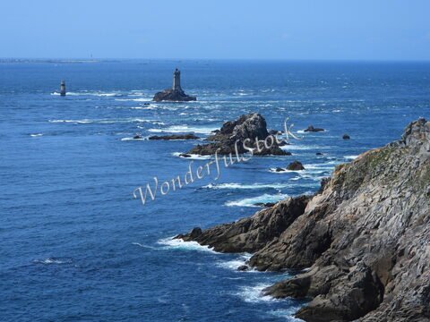 Rochers et phares au large de la Pointe du Raz, en Bretagne, France, avec une mer calme et un ciel dégagé.