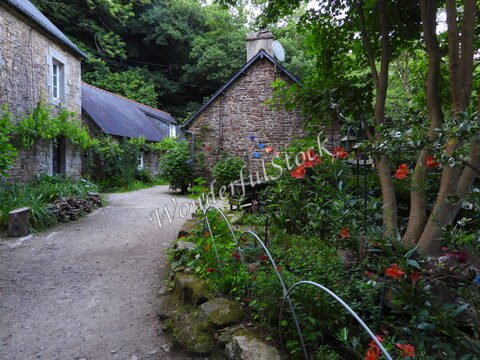 Un chemin bordé de fleurs et de verdure, menant à des maisons en pierre à Pont-Aven, Bretagne, France.