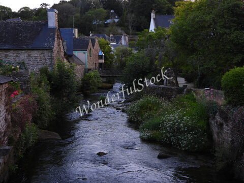 Rivière bordée de maisons en pierre et de verdure à Pont-Aven, France. Des fleurs colorées ajoutent une touche de vie au paysage.
