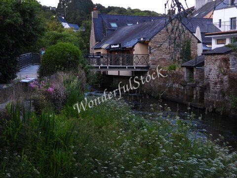 Un pont en bois surplombe un cours d'eau, entouré de maisons en pierre et de fleurs à Pont-Aven, Bretagne, France.