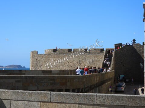 Murs en pierre avec des visiteurs à Saint-Malo, France, sous un ciel bleu, avec la mer visible en arrière-plan.