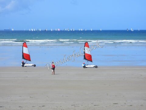 Des chars à voile sur la plage de Sainte-Anne-la-Palud en Bretagne, France, avec des voiles rouges et blanches et un paysage marin en arrière-plan.