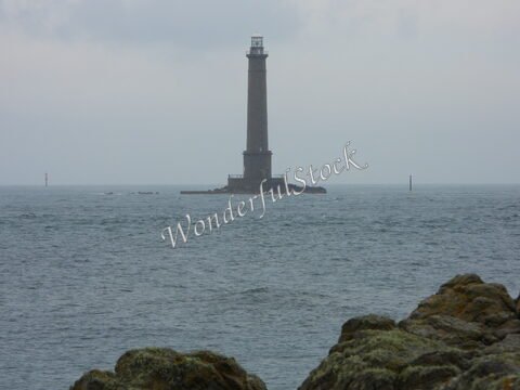 Phare au large de la Bretagne, France, se dressant sur un rocher dans une mer agitée, avec des pierres en premier plan.