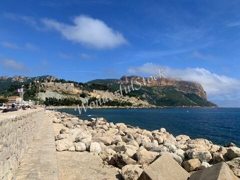 Cassis, France, avec des rochers au bord de l'eau et une colline boisée en arrière-plan.