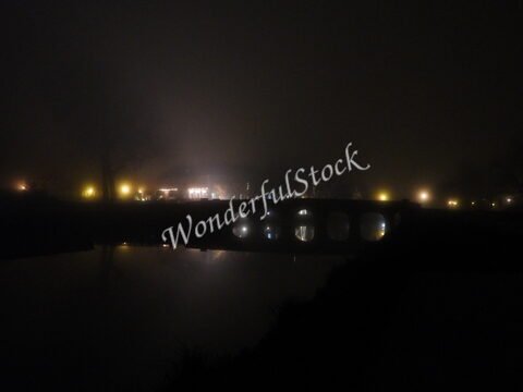 Pont éclairé au bord d'un cours d'eau dans la brume à Chambord, France.