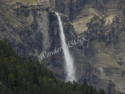 Cascade d'eau dans le cirque de Gavarnie, France, entourée de falaises rocheuses et de forêts verdoyantes.