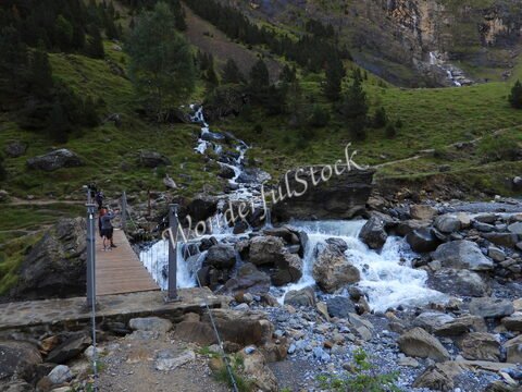 Ruisseau et pont en bois dans le cirque de Gavarnie, France, avec des rochers et de la verdure environnante.
