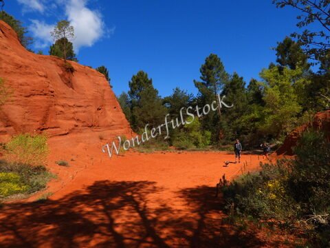 Terrain rouge entouré de roches et de végétation dans le Colorado provençal, France. Des personnes se déplacent sur le sol sablonneux.