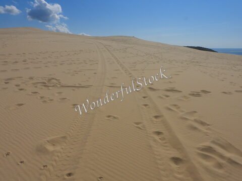 Dune de sable à la Dune du Pilat, France, avec des traces de pas et un ciel bleu partiellement nuageux.