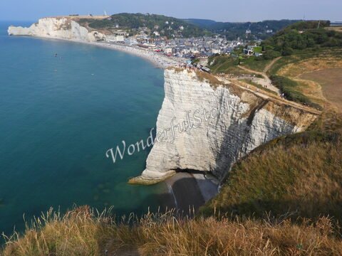 Falaises blanches surplombant la mer à Étretat, France, avec une plage animée et des maisons en arrière-plan.