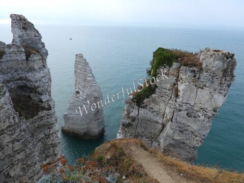 Falaises blanches surplombant la mer, à Étretat, France, avec des formations rocheuses distinctives et un ciel nuageux.