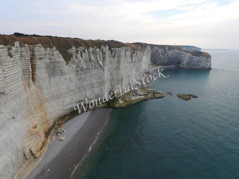 Falaises blanches sur la plage à Étretat, France, avec la mer en arrière-plan et un ciel légèrement nuageux.