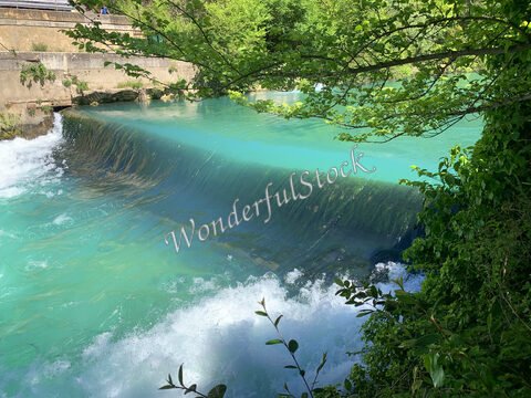 Cascade d'eau turquoise à Fontaine du Vaucluse, France, entourée de verdure et de rochers.