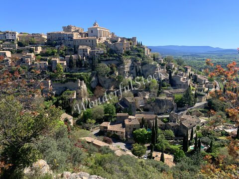 Village perché à Gordes, France, avec des bâtiments en pierre et des cyprès, surplombant la vallée environnante.
