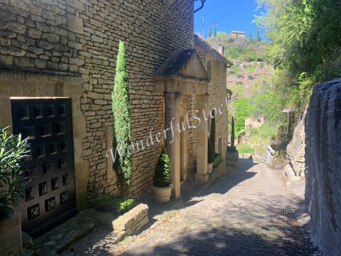 Rue pavée avec des maisons en pierre et des cyprès à Gordes, France.