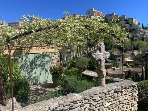 Croix en pierre avec un ciel bleu, entourée de maisons en pierre à Gordes, France.