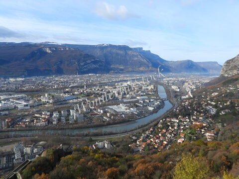Vue panoramique de la ville de Grenoble, France, avec des montagnes en arrière-plan et la rivière Isère serpentant à travers l'agglomération.