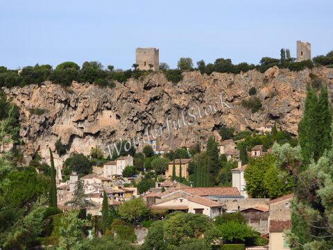 Village au pied de falaises, avec des maisons colorées, situé dans le Haut Var, France. Deux tours se dressent au sommet des rochers.