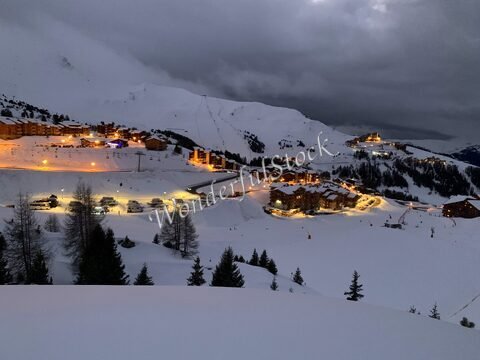 Stations de ski illuminées dans la neige à La Plagne, France, avec des montagnes en arrière-plan et un ciel nuageux.