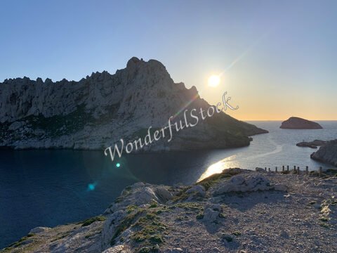 Coucher de soleil sur les calanques à Marseille, France, avec des rochers escarpés et une mer calme.