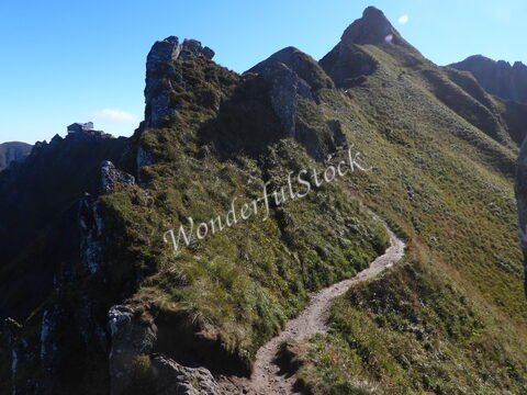 Chemin sinueux sur une crête verdoyante à Mont-Dore, France, avec une construction visible en arrière-plan.