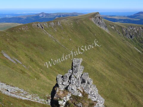 Roc au sommet d'une colline verdoyante à Mont-Dore, France, avec des paysages montagneux en arrière-plan.