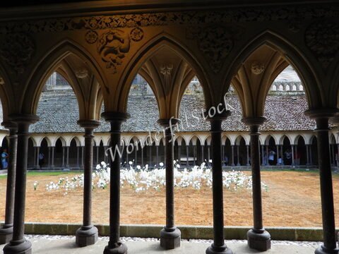 Cloître avec arches, fleurs blanches et pelouse sèche au Mont Saint-Michel, France.