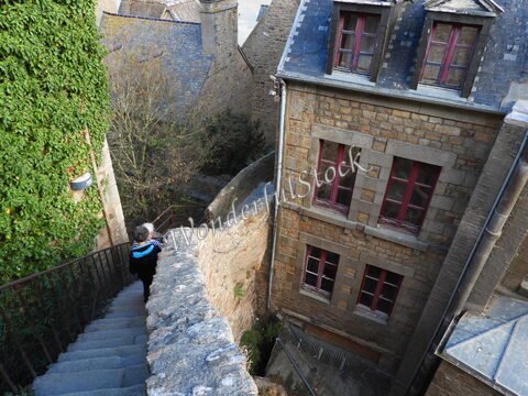 Escalier en pierre à Mont Saint-Michel, France, avec des maisons en pierre et des fenêtres à rideaux rouges.