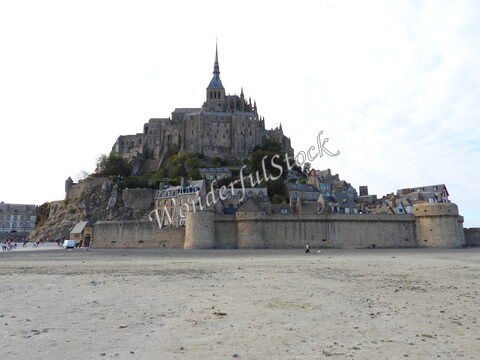 Mont Saint-Michel, France, avec ses murs en pierre et son abbaye surplombant le paysage, entouré de sable.