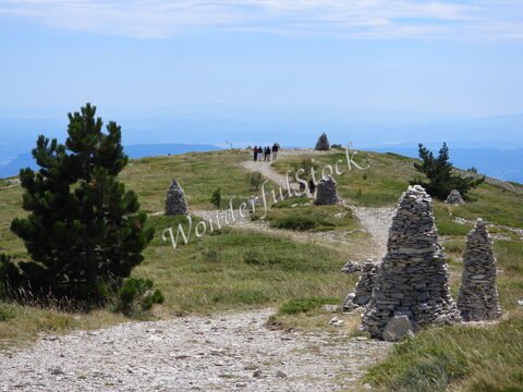 Sentier menant au Mont Ventoux en France, avec des cairns en pierre et des promeneurs sur une prairie verdoyante.