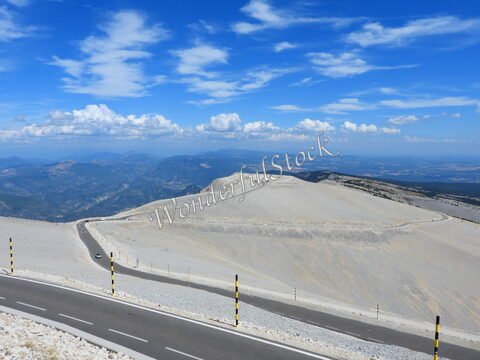 Mont Ventoux en France, avec une route sinueuse sur un terrain aride et des nuages épars dans un ciel bleu.