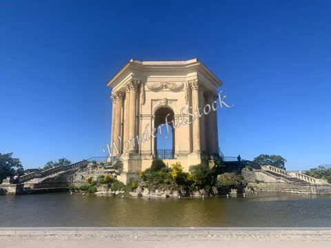 Monument emblématique au bord de l'eau à Montpellier, France, avec des colonnes et un ciel bleu clair.