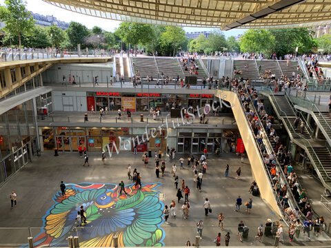 Un espace animé avec des personnes et un sol coloré à Paris, France, sous une structure architecturale moderne.