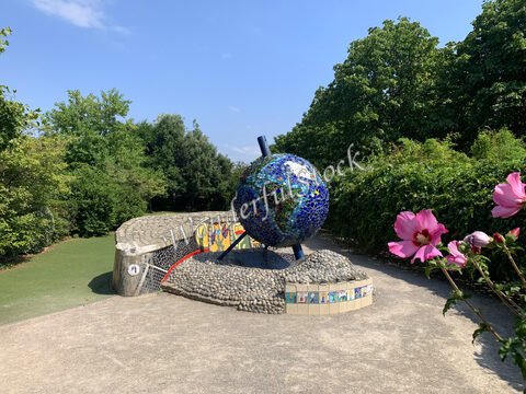 Globe en mosaïque dans un parc à Paris, France, entouré de verdure et de fleurs.