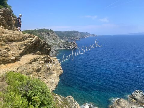 Un homme se tient sur une falaise sur l'île de Porquerolles, France, surplombant la mer bleue et des rochers escarpés.