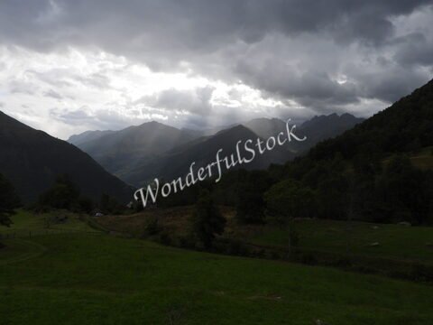 Paysages montagneux dans les Pyrénées, France, avec des nuages sombres et des rayons de lumière perçant à travers.