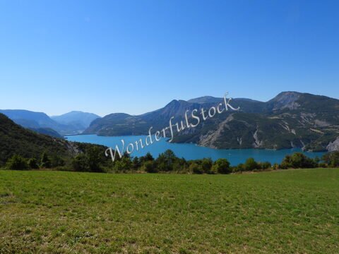 Lac de Serre-Ponçon en France, entouré de montagnes, avec un ciel bleu et une verdure au premier plan.