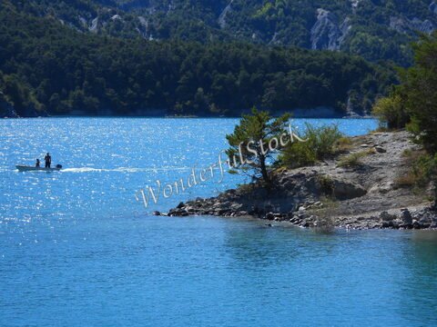 Un bateau navigue sur le lac de Serre-Ponçon en France, entouré de collines verdoyantes et d'une plage rocheuse.