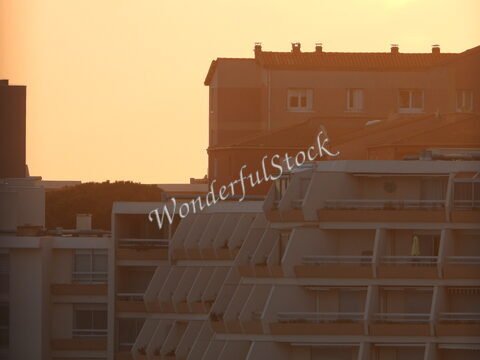 Bâtiments résidentiels à Sète, France, avec des balcons et des fenêtres, sous un ciel orangé au coucher du soleil.