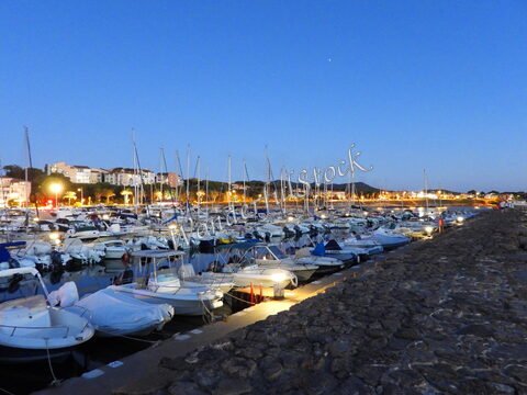 Bateaux amarrés dans le port de Six-Fours, France, éclairés par des lumières nocturnes et entourés de bâtiments en arrière-plan.