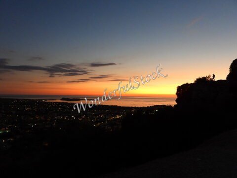 Coucher de soleil sur la mer à Six-Fours, France, avec des lumières de la ville en arrière-plan et des silhouettes sur la colline.