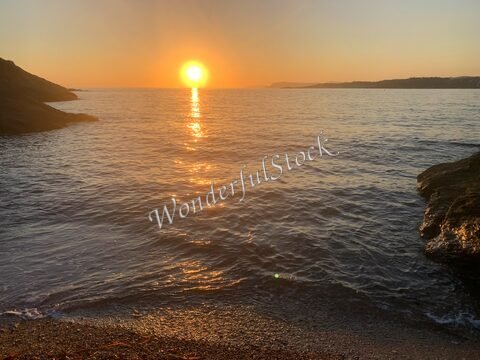 Coucher de soleil sur la mer à Six-Fours, France, avec des rochers au premier plan et des reflets dorés sur l'eau.