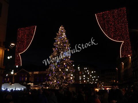 Un grand sapin de Noël illuminé sur une place à Strasbourg, France, entouré de décorations lumineuses et de visiteurs.