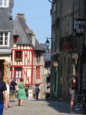 Ruelles pavées de Dinan, France, entourées de maisons à colombages et de boutiques, avec des passants et un ciel dégagé.