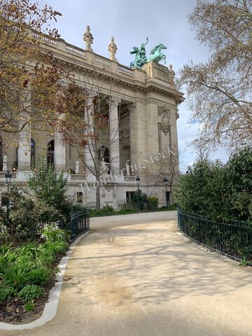 Bâtiment avec des sculptures équestres et des colonnes, à Paris, France, entouré de verdure et de chemins en terre.