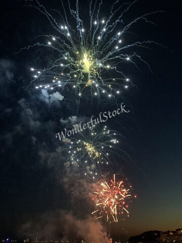 Feux d'artifice illuminant le ciel nocturne à Sanary, France, avec des éclats de lumière colorés et de la fumée.