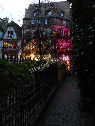 Maison décorée avec des lumières de Noël dans une ruelle à Strasbourg, France, avec un mur de pierre et une clôture en fer.