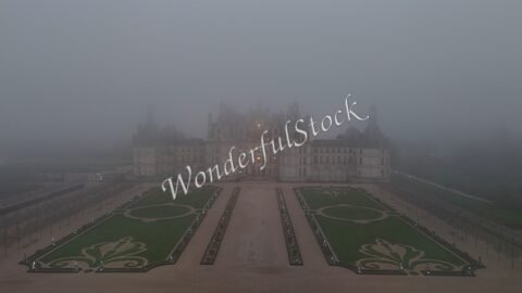 Château de Chambord en France, entouré de brouillard, avec des jardins symétriques visibles au premier plan.