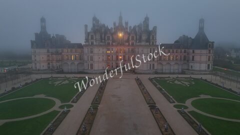 Château de Chambord en France, vu sous un brouillard, avec un jardin soigné et des illuminations décoratives.