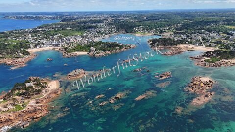 Ploumanach, France, avec ses côtes rocheuses et ses eaux turquoise, entouré de maisons blanches et de bateaux dans le port.